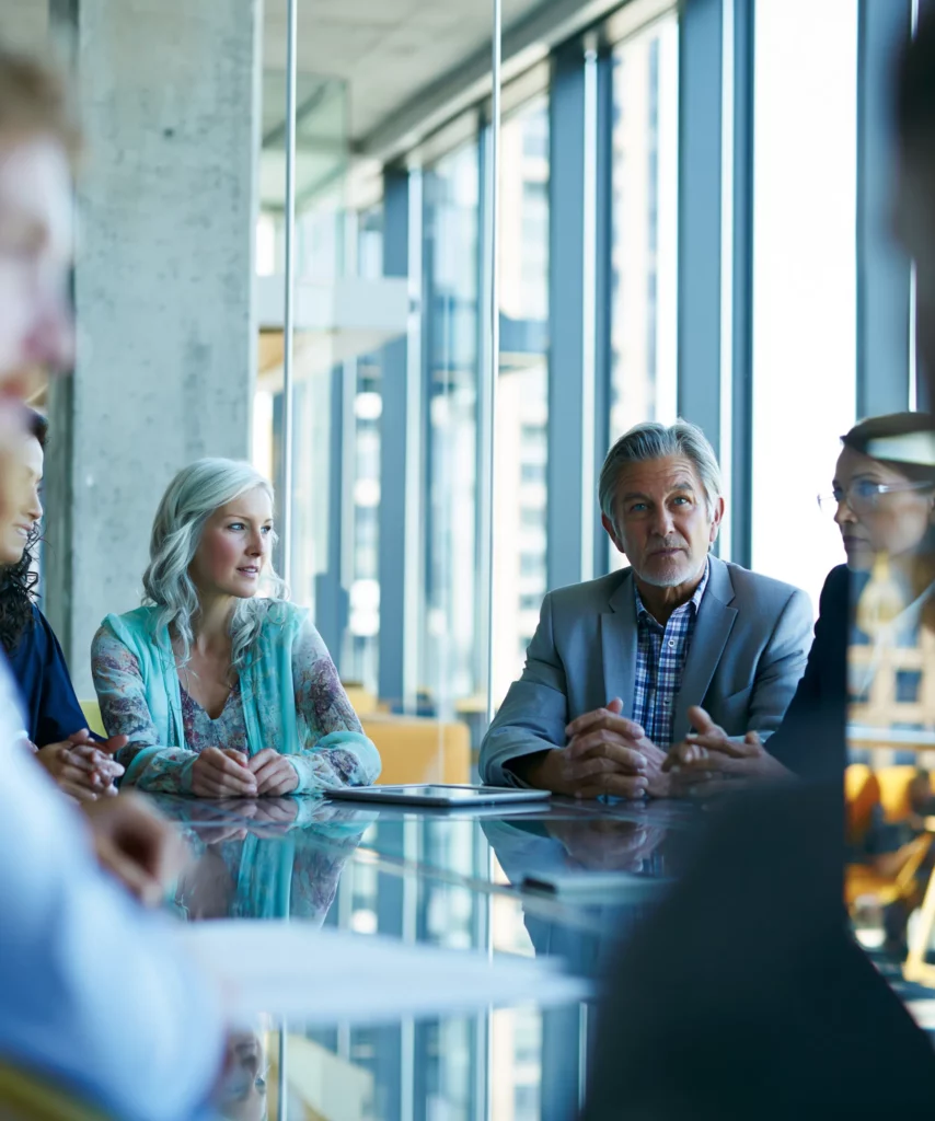 Famille dirigeante multigénérationnelle réunie autour d'une table en verre dans un bureau contemporain, illustrant la gouvernance familiale d'entreprise