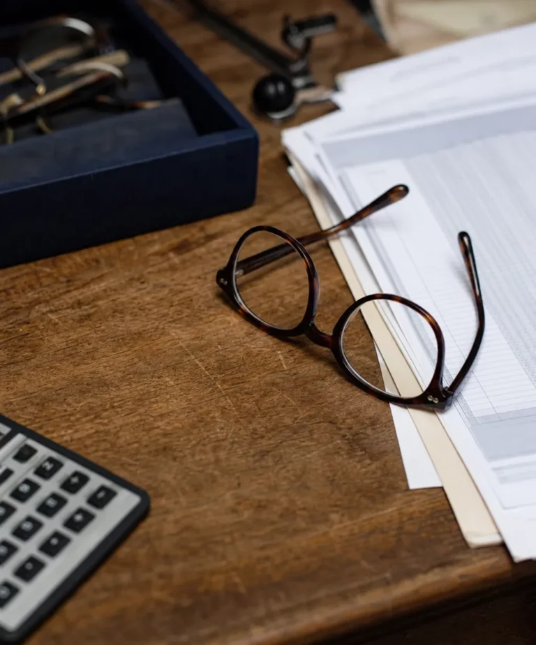 Lunettes posées sur des documents comptables et une grille tarifaire, symbole de la pression de la taxe OCAM sur la marge de l'opticien