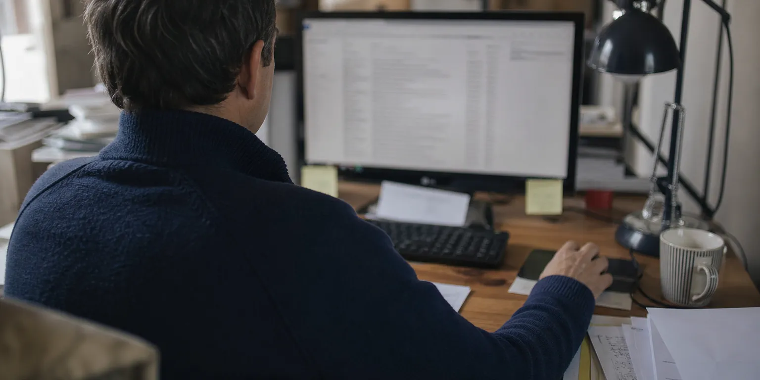 Gérant d'entreprise hésitant devant sa boîte mail professionnelle, illustrant la vérification d'un courriel suspect prétendument envoyé par les impôts