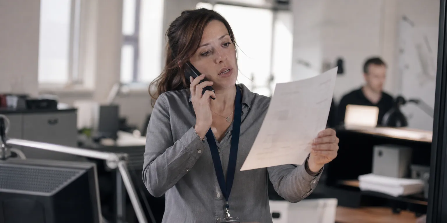 Assistante comptable vérifiant par téléphone une facture fournisseur, illustrant la prévention de la fraude au virement et au faux changement de RIB