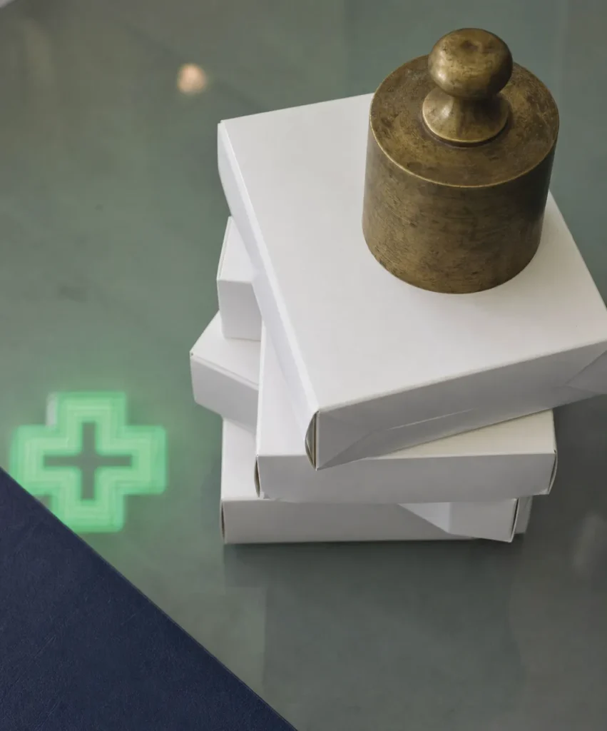 Boîtes de médicaments génériques maintenues par un presse-papier, symbole des plafonds de remises génériques gravés dans la loi