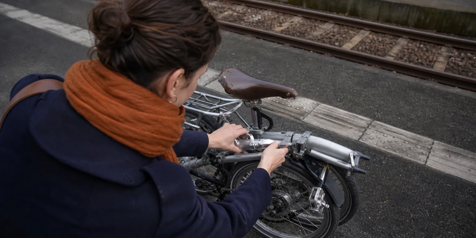 Salariée pliant son vélo sur un quai de gare TER : cumul du forfait mobilités durables et de l'abonnement transport